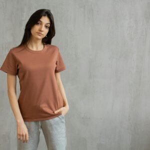 Serious female with long hair wearing t shirt and sweatpants standing against gray wall and looking at camera